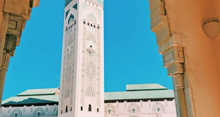 El imponente minarete de la Mezquita Hassan II enmarcado por un arco contra un cielo turquesa despejado.