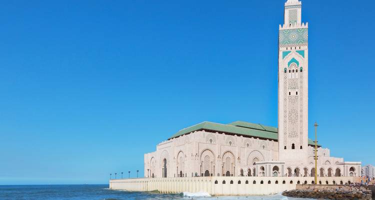 Ángulo junto al mar de la Mezquita de Hassan II con olas suaves rompiéndose contra el muro de piedra.