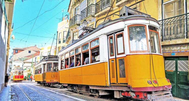 Twee vintage gele trams die door een smalle, kleurrijke straat in Lisboas Alfama-wijk navigeren.