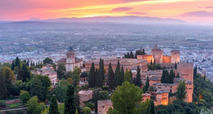 Vista panorámica al atardecer de la fortaleza de la Alhambra rodeada de cipreses con vistas al valle de Granada.