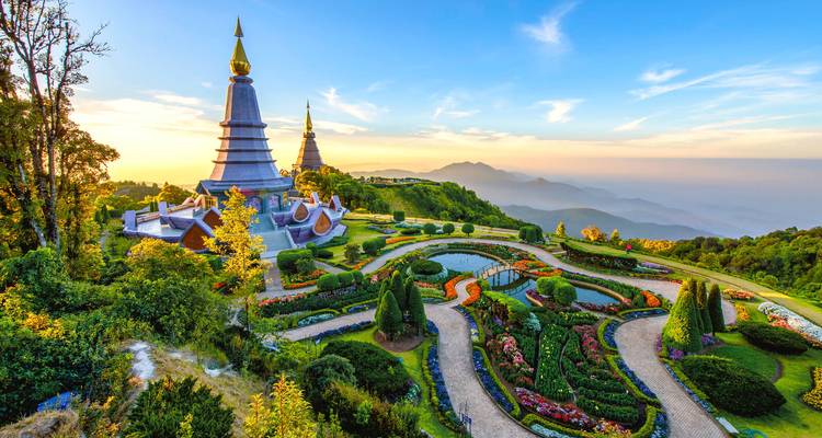 Zwillingspagodan von Doi Inthanon erheben sich bei goldenem Sonnenaufgang über gepflegten königlichen Gärten vor nebligem Bergpanorama.