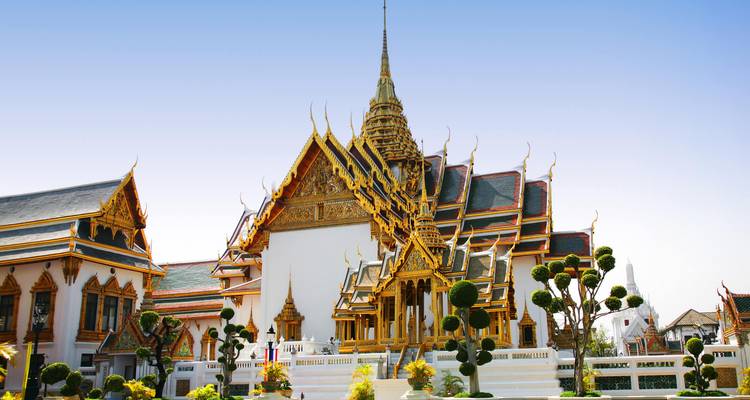 Der kunstvoll verzierte, mit goldenem Dach versehene Thronsaal und die Tempel des Großen Palastes von Bangkok glänzen unter klarem blauem Himmel.