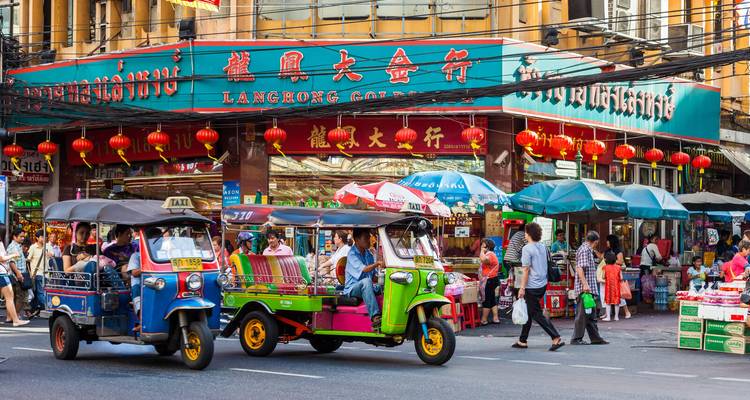 Lebendige Bangkok-Chinatown-Straßenszene mit farbenfrohen Tuk-Tuks, neonbeleuchteten chinesischen Zeichen und Fußgängern.
