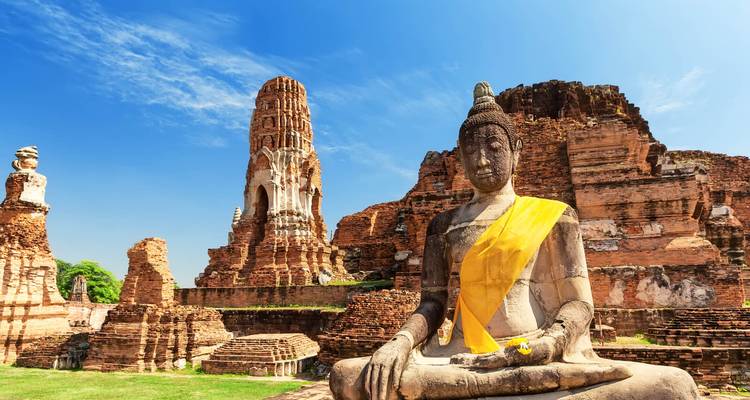 Ruhiger sitzender Buddha und Backsteinprang inmitten der Ruinen von Ayutthaya unter blauem Himmel.