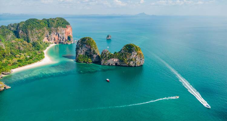 Luftaufnahme eines Panoramas kleiner tropischer Inseln und Schnellboote, die weiße Kielwasser über tiefblauen Meer durchziehen.