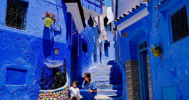 Woman and child sitting on a mosaic bench along a vivid blue alley in Chefchaouen’s medina, Morocco.