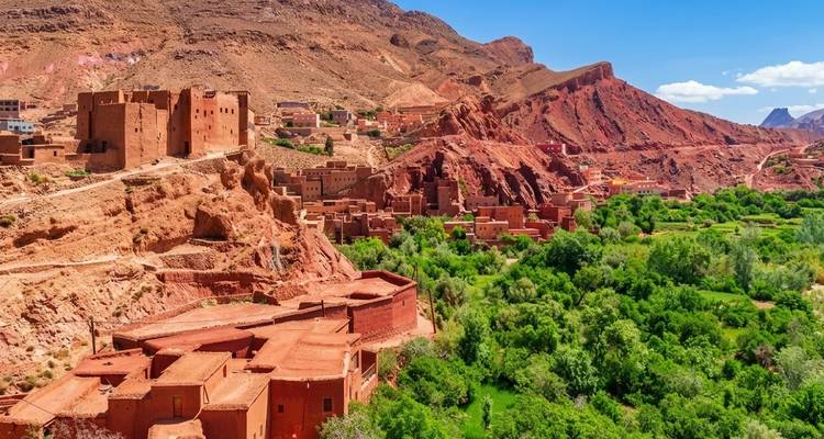 Earthen kasbah villages perched on red hills above a lush green valley in southern Morocco.