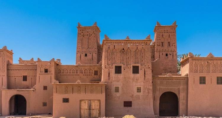 Front façade of a traditional adobe kasbah with decorative towers under a clear blue sky.