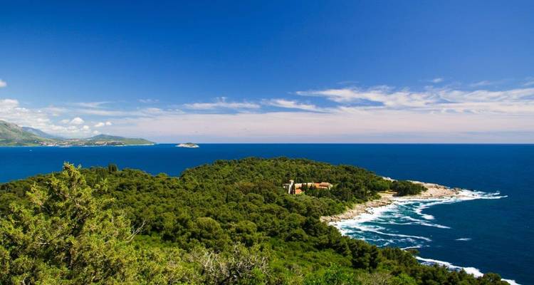 La isla de Lokrum, cubierta de bosques, se encuentra en el azul Adriático rodeada de una costa escarpada y olas que se estrellan.