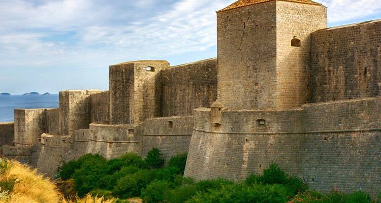 Los enormes muros de piedra y bastiones de las fortificaciones medievales de Dubrovnik se elevan sobre la vegetación y el mar.