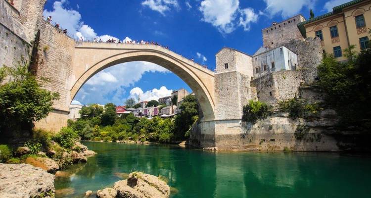 El icónico arco de piedra del puente Stari Most de Mostar se extiende sobre el río Neretva de color esmeralda bajo un cielo azul brillante.