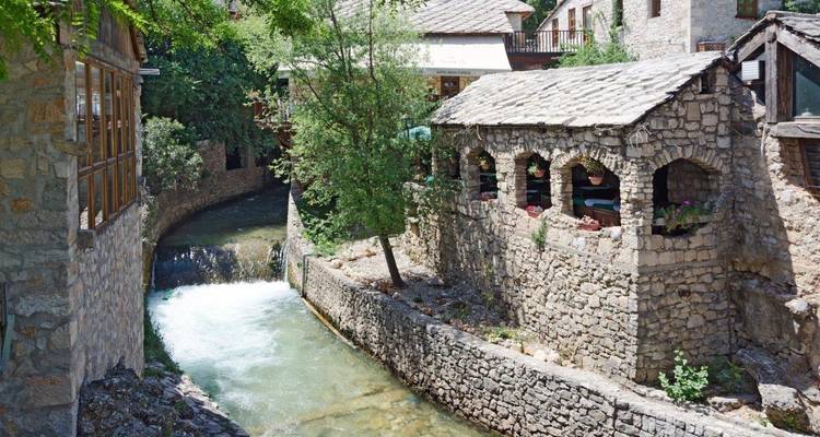 Los molinos de piedra bordean un arroyo estrecho con agua en cascada que fluye a través de un pueblo bosnio histórico.
