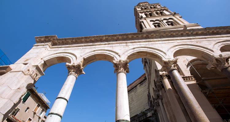 Ángulo hacia arriba de los arcos de mármol y la alta torre campanario de la Catedral de San Dalmacio de Split contra el cielo azul.