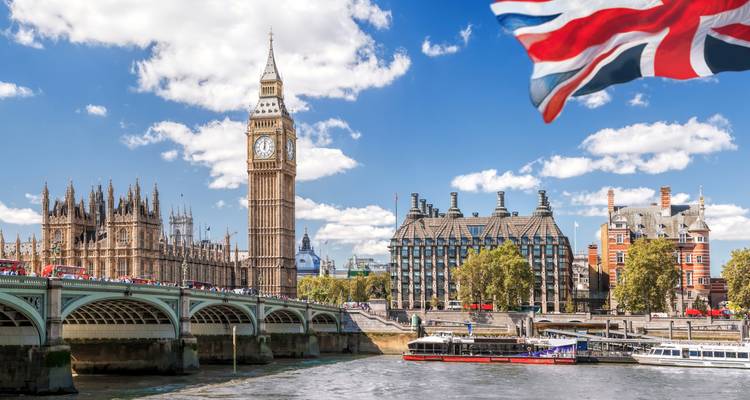 Vista icónica de Big Ben y las Casas del Parlamento desde el Río Támesis bajo un cielo despejado con la bandera de la Unión Jack.