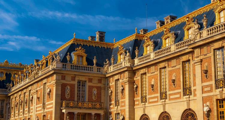 La luz dorada del atardecer iluminando la fachada ornamentada y las estatuas del Palacio de Versalles.