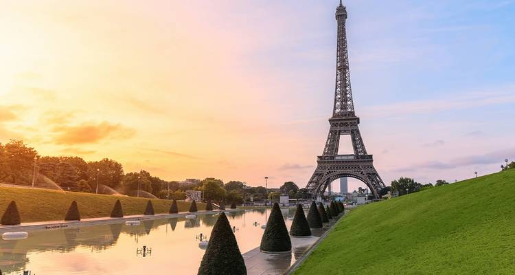 La Tour Eiffel s'élevant à côté d'un bassin de réflexion au lever du soleil avec des couleurs de ciel pastel.