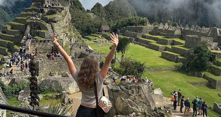 Jeune femme levant les bras en signe de triomphe devant la vue panoramique des ruines du Machu Picchu.