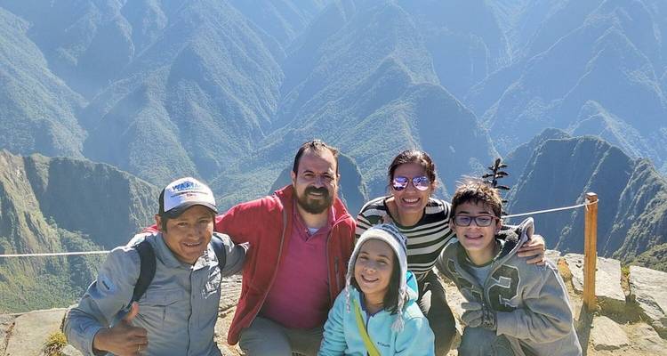 Un groupe familial sourit depuis un belvédère montagneux surplombant les vallées verdoyantes et accidentées de la région du Machu Picchu.