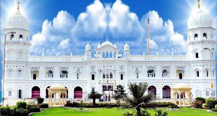Cliché de jour lumineux d'un temple sikh blanc orné encadré par un ciel bleu éclatant parsemé de nuages et d'une pelouse bien entretenue à l'avant.