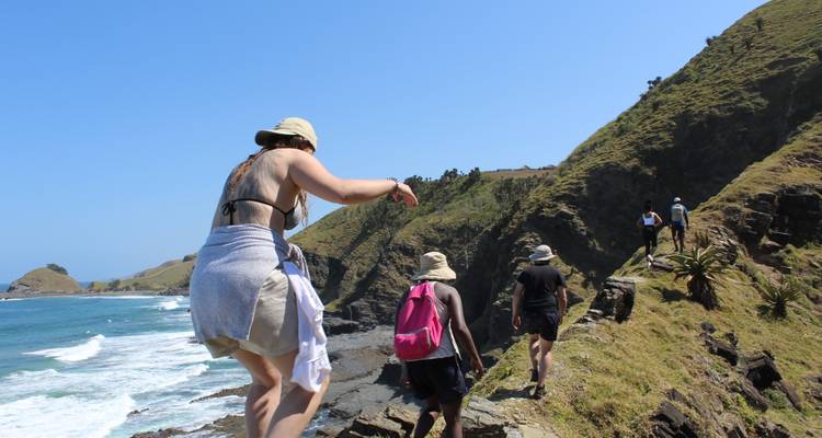 Los excursionistas atraviesan cuidadosamente un estrecho sendero de acantilado costero sobre olas que se estrellan.