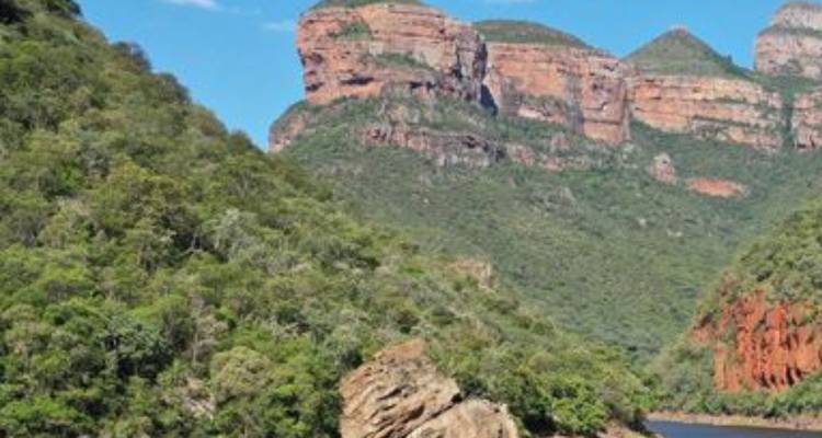 Las empinadas paredes del cañón verde se alzan sobre un río sinuoso bajo un cielo azul despejado.
