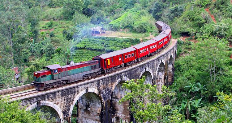 El icónico tren rojo y verde cruzando el Puente de Nueve Arcos de piedra en medio de exuberantes plantaciones de té en Sri Lanka