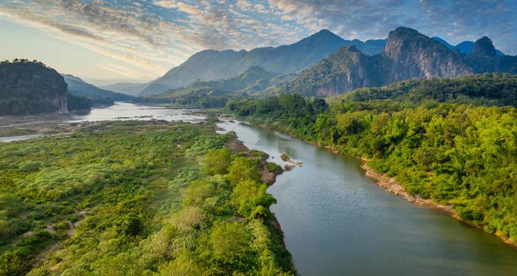 Valle verde y exuberante con río sinuoso y dramáticas montañas de piedra caliza bajo nubes con patrones