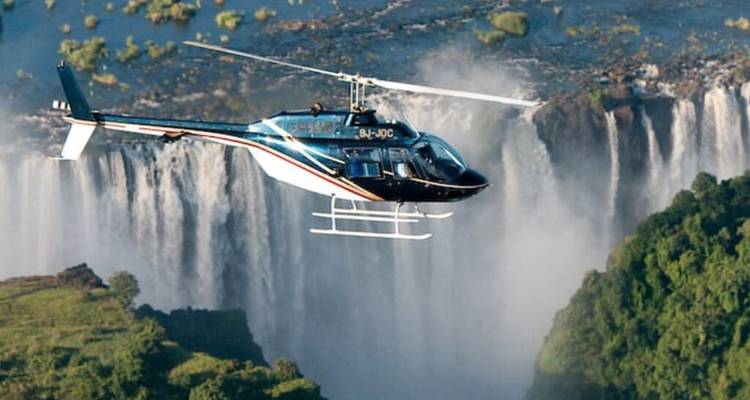 Hubschrauber, der über die Schlucht der Viktoriafälle fliegt, mit aufsteigenden Wassernebel im Hintergrund