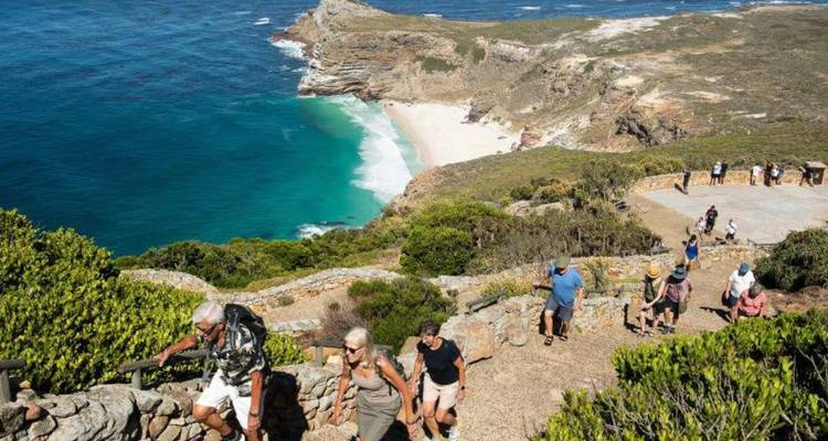 Los excursionistas suben escalones de piedra sobre una bahía turquesa y acantilados costeros espectaculares.
