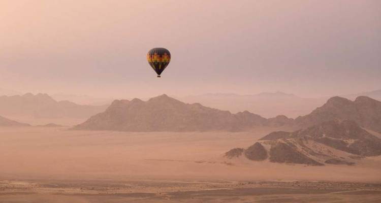 Un solitario globo aerostático flota sobre las vastas llanuras desérticas de colores pastel al amanecer.