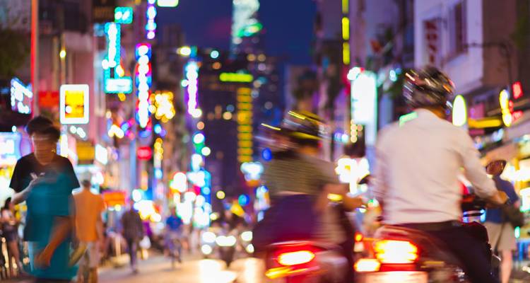Nächtliche Straßenszene mit Neonlichtern und unscharfen Motorrädern im regen Straßenverkehr einer vietnamesischen Stadt