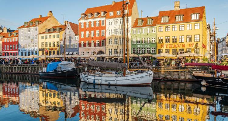 Las coloridas casas de tejados triangulares de Nyhavn se reflejan vívidamente en el tranquilo canal junto a los barcos amarrados.