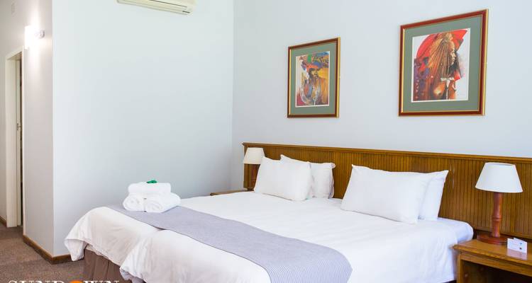 Habitación de hotel con dos camas individuales bien ordenada, con cuadros enmarcados y toallas dobladas colocadas sobre la manta.