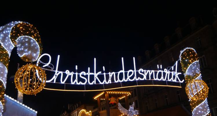 Panneau lumineux affichant « Christkindelsmärik » en arc de cercle au-dessus d'une rue festive la nuit.