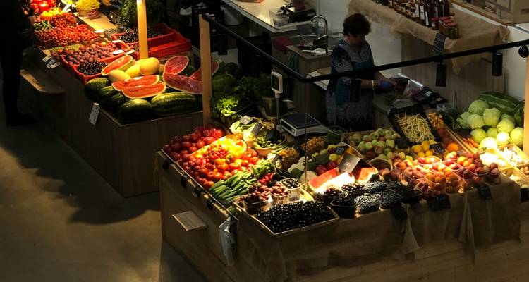 Markttand in der Halle, erleuchtet über Stapeln von farbenfrohem frischem Gemüse und Obst