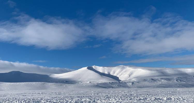 Colinas de nieve blancas e impolutas como dunas bajo un cielo azul con algunas nubes dispersas.