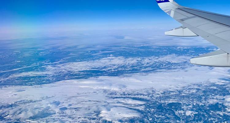 Vista aérea desde el ala del avión sobre un extenso paisaje cubierto de nieve bajo una atmósfera azul cristalina.