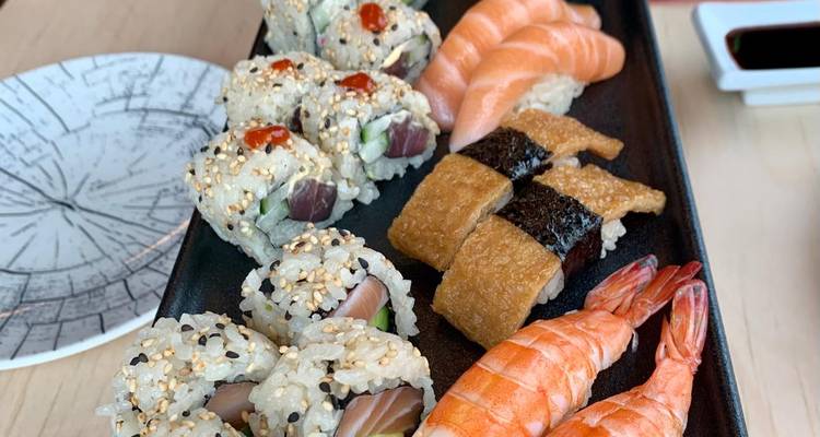 Variados rollos de sushi, nigiri y camarones cuidadosamente arreglados en una fuente negra en un restaurante.