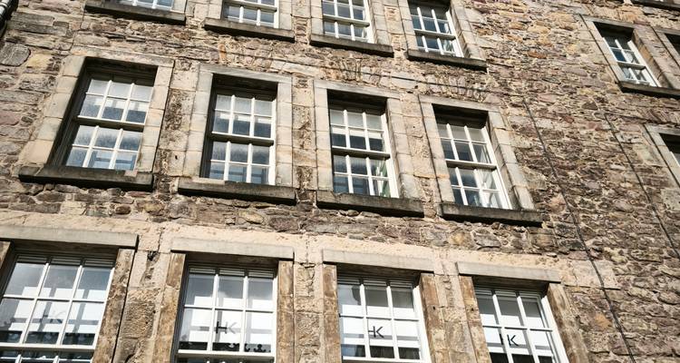 Primer plano de la fachada de un edificio antiguo de piedra con hileras de ventanas de guillotina.