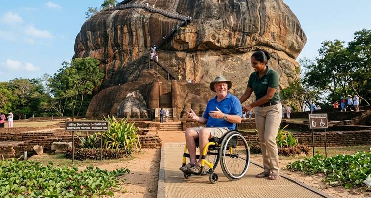 Visitante en silla de ruedas y guía en la base de la icónica Roca de Sigiriya en Sri Lanka, con la enorme fortaleza elevándose dramáticamente detrás.