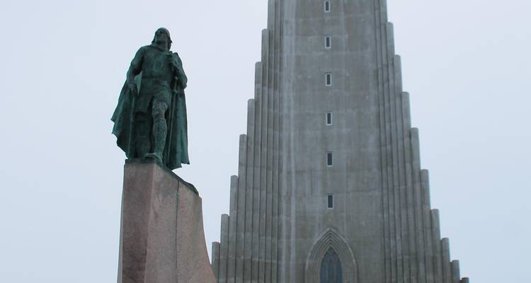Standbeeld van Leif Erikson voor de imposante betonnen gevel van de Hallgrimskirkja-kerk op een bewolkte dag.