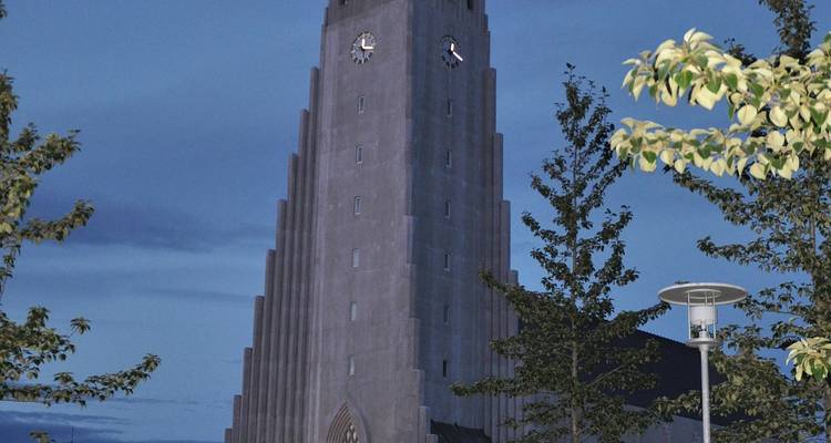 Hallgrimskirkja-kerk verlicht in de schemering met een diepblauwe avondschemering en omringende bomen.