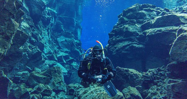 Plongeur en apnée équipé complètement explorant une fissure sous-marine d'un bleu cristallin entourée de parois rocheuses escarpées.