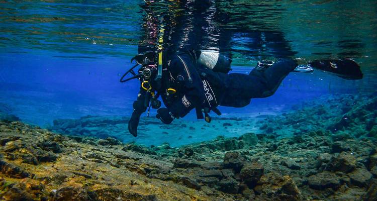 Vue latérale d'un plongeur en apnée glissant au-dessus d'un terrain rocheux dans une eau bleue exceptionnellement limpide.