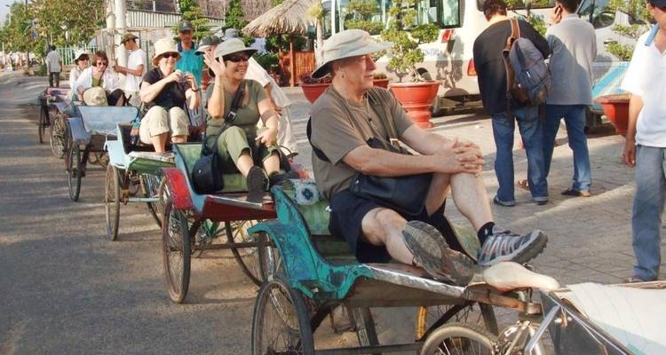 Touristen fahren in einem Konvoi mit Fahrradrikschas eine sonnige Straße entlang.