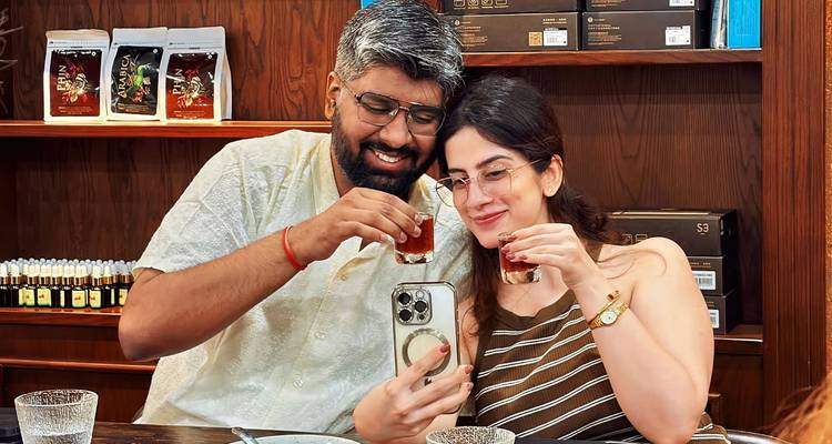 Pareja sonriente brindando con pequeños vasos de café mientras se toman una selfie en una cafetería.
