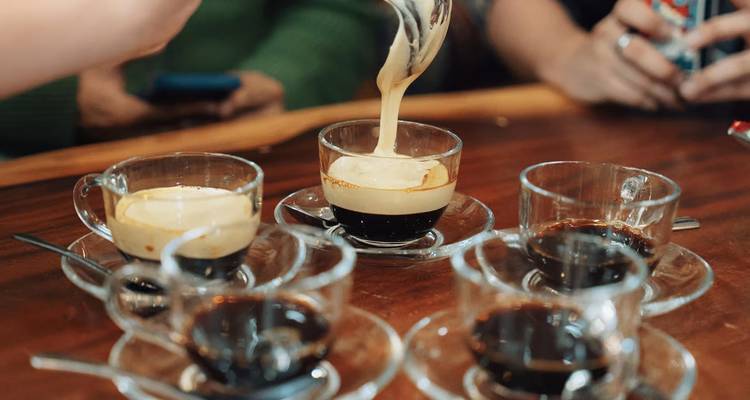 Primer plano de café de huevo vietnamita siendo vertido en pequeñas tazas de vidrio sobre una mesa.