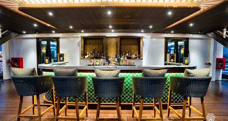 Bar elegante del crucero con mostrador de azulejos verdes y taburetes altos bajo los focos.