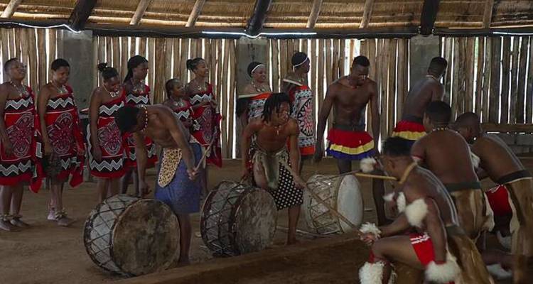 Bailarines y percusionistas tradicionales swazi actuando dentro de una cabaña cultural con techo de paja