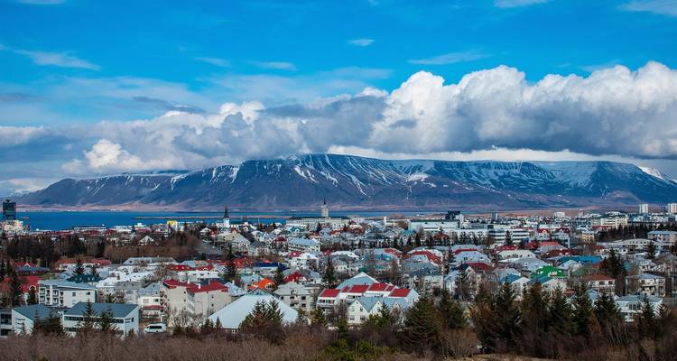 Panorama de Reikiavik con cadena montañosa cubierta de nieve y un dramático manto de nubes sobre la ciudad.